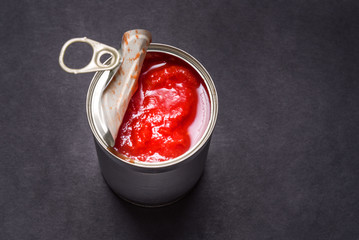 Opened tin can with canned tomatoes, on black background