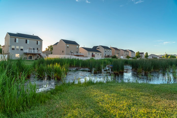Fototapeta na wymiar Pond with green grassy shore and multi storey family homes in the background