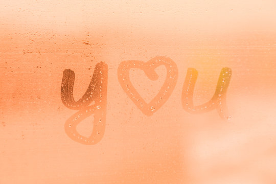 The romantic inscription I love you on the orange or pink evening or morning window glass with drops 