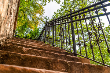 Close up of staircase with stone treads and metal railing against leaves and sky