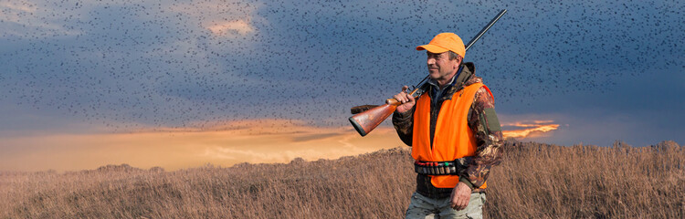 A hunter with a gun in his hands in hunting clothes in the autumn forest in search of a trophy. A man stands with weapon. © Mountains Hunter
