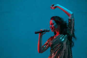 Caucasian female singer portrait isolated on blue studio background in neon light. Beautiful female...