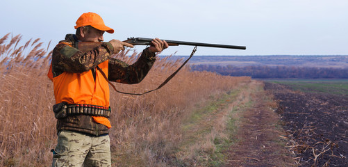 A hunter with a gun in his hands in hunting clothes in the autumn forest in search of a trophy. A...