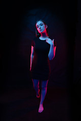beautiful girl in a black dress. light of colored lamps of blue red colors. Girl stands in full growth. on a black background Fashion contemporary neon portrait. Adorable fashionable sexy model girl