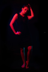 beautiful girl in a black dress. In the light of colored lamps of in red, bright light and outline blue. Girl stands in full growth. on a black background