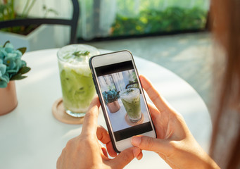 An Asian woman uses a smartphone to take pictures of green tea in a cafe.