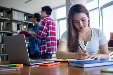 Asian female students sit and do their homework in the library.