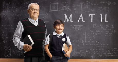 Schoolboy and an elderly male teacher posing in front of a blackboard with written text math and formulas