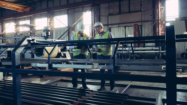Metal-processing conveyor and two workers observing it