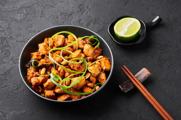 Kung Pao Chicken or Gong Bao Ji Ding at dark slate background. Sichuan Kung Pao is chinese cuisine dish with chicken meat, chilli peppers, peanuts, sauces and onion.