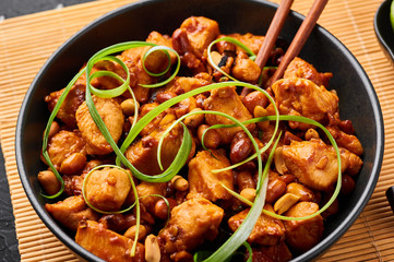 Kung Pao Chicken or Gong Bao Ji Ding at dark slate background. Sichuan Kung Pao is chinese cuisine dish with chicken meat, chilli peppers, peanuts, sauces and onion.