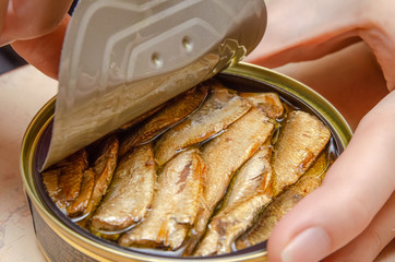 Female hands open a can of fish sprats on the table close up