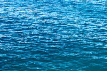 Clear water texture in blue. Background of the ocean and the sea backlit by the sun.
