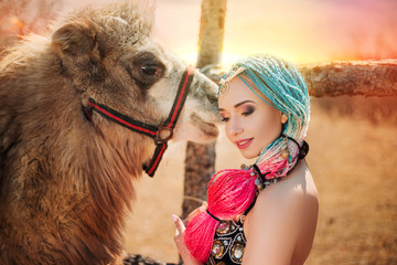 Obraz premium Beautiful girl with multi-colored braids in oriental clothes. Princess with a camel at sunset. in desert
