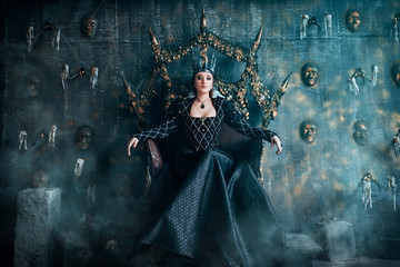 Fototapeta premium Evil Queen w czarnej sukience. Piękna dziewczyna w koronie siedzi na tronie