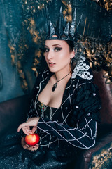 Evil Queen in a black dress. Beautiful girl in the crown sits on the throne