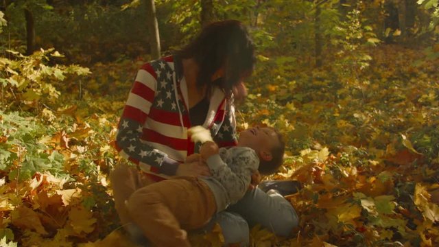 A young Caucasian woman tickles her son in autumn leaves. Recorded in Raw on Blackmagic camera.