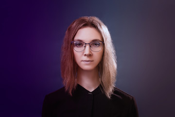 Portrait of a young beautiful girl with glasses in neon light. Serious expression, blue eyes