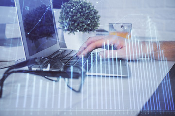 Multi exposure of graph with man typing on computer in office on background. Concept of hard work. Closeup.