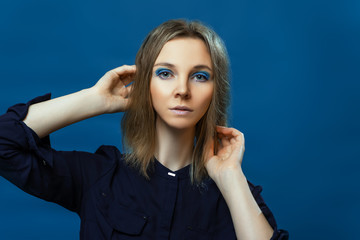 Portrait of a young beautiful girl on a blue background. Fashionable girl straightens her hair.
