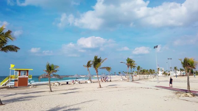 Pan of Picturesque Beach at Al Mamzar Park in Dubai With People Under Umbrellas and Palm Trees Scattered Throughout Frame