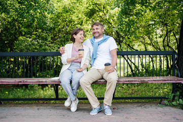 Middle-aged married couple drink coffee on the bench.