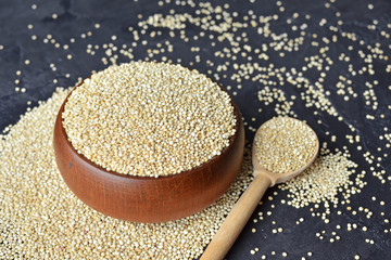 Organic quinoa grains in wooden bowl and spoon on dark stone background. Cooking ingredients, healthy food.