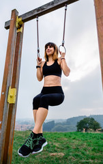 Female athlete doing gymnastic rings exercises in a park