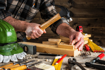 Close-up. Carpenter with hammer and nails fixes a wooden board. Construction industry, do it yourself. Wooden work table.