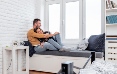 Young couple in love enjoying time together at home sitting by the window and relaxing in apartment.