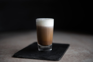 mini cup of cappuccino in a glass cup on black background and light table