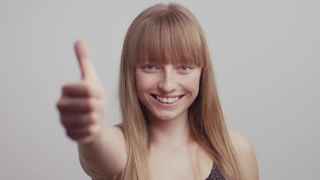 Potrait shot of happy Woman in studio giving positive thumps up sign with hand,slow motion