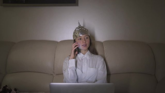 Tin Foil Hat protects woman`s brain from 5G waves, internet, electromagnetic fields, mind control. Girl speaks on the phone.