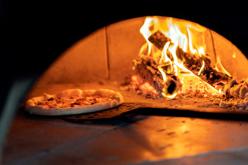 Pizza in the oven on a shovel near the burning wood