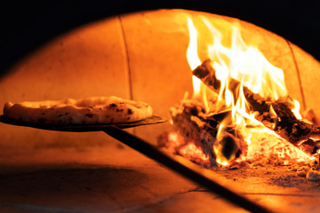 Pizza in the oven on a shovel near the burning wood