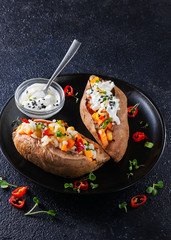 Baked sweet potato or yam, stuffed with chickpeas, rice, vegetables, red chilli pepper and yogurt sauce dressing. Overhead view, dark background with copy space. Healthy vegan food concept.