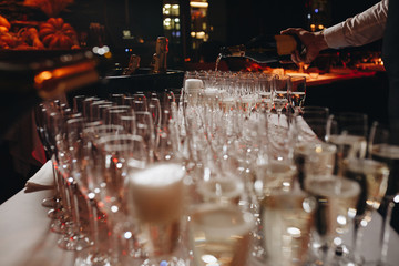 Bartender pouring champagne or wine into wine glasses on the table at the outdoors solemn wedding ceremony