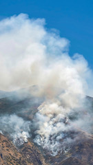 Vertical Aerial view of mountain with white smoke from wild forest fire on a sunny day