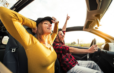 Happy couple in love driving a convertible car at sunset on the road