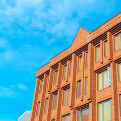 Fototapeta na wymiar Square Commercial building with red brick wall viewed against blue sky and clouds