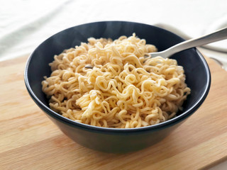 Instant noodles with fork on a black bowl. Selective focus.