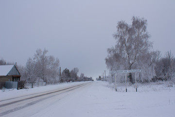 A snow-covered house and trees on the outskirts of a Russian village, the inscription 