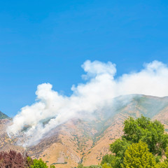 Square frame Clear blue sky over mountain slopes with puffs of smoke from a wild forest fire