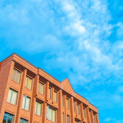 Square frame Commercial building with red brick wall viewed against blue sky and clouds