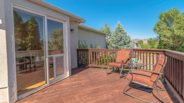Pano Wooden balcony with metal armchairs facing the sliding glass door of a home