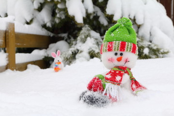 Felt figurines of a snowman and happy bunny on the background of a snowy pine tree and hedge.