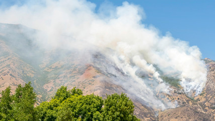 Naklejka premium Pano frame White smoke over mountain peak with green tree leaves on a sunny day