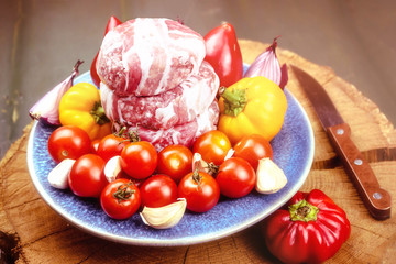 Meat raw round cutlets wrapped in bacon and vegetables onion, sweet pepper, garlic on a blue clay plate. Ingredients for cooking meat dishes. The concept of meat-lovers