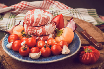 Meat raw round cutlets wrapped in bacon and vegetables onion, sweet pepper, garlic on a blue clay plate. Ingredients for cooking meat dishes. The concept of meat-lovers. Toned.