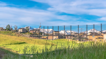 Fototapeta na wymiar Pano Golf course scenic views on a sunny day with homes and snow capped mountain